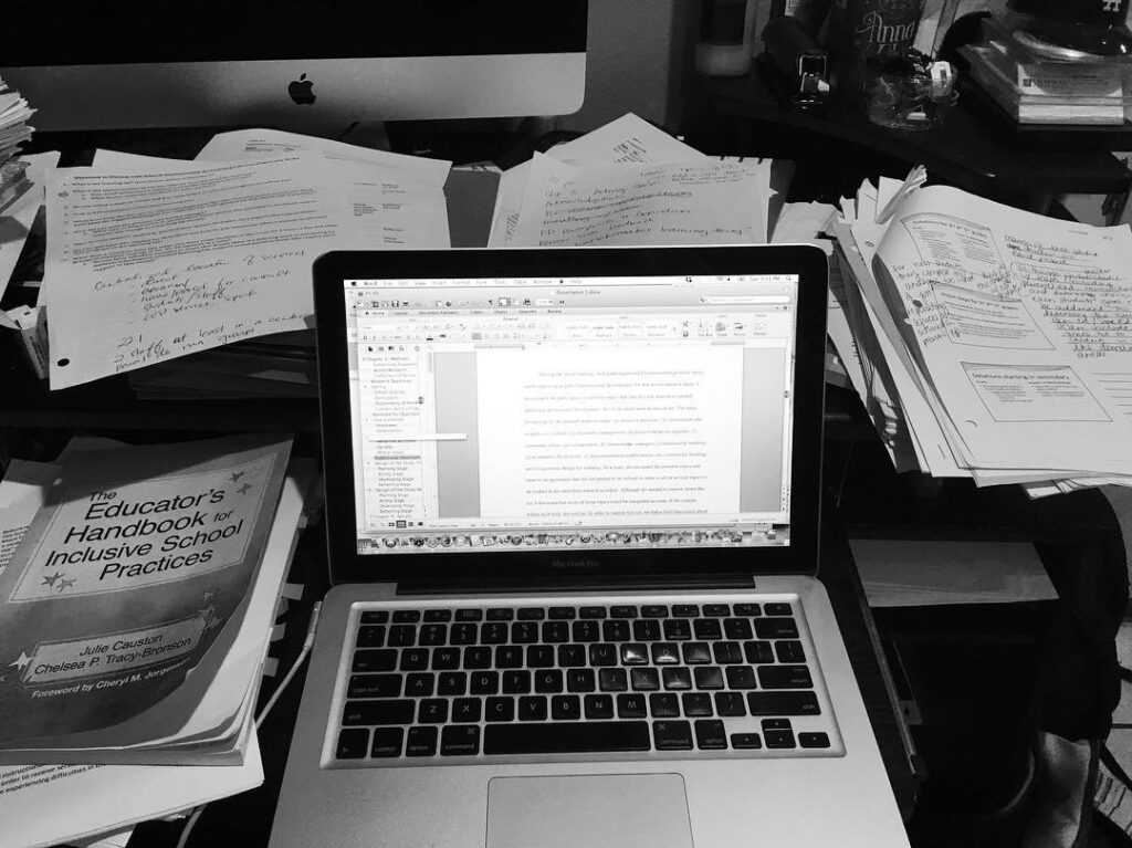 Computer surrounded by papers and books